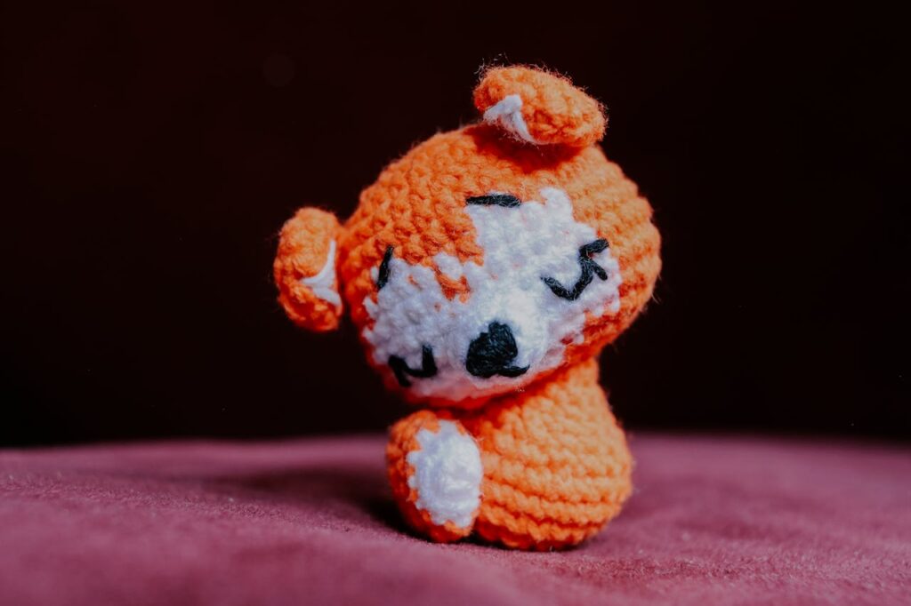 Adorable handmade orange crochet animal figure on a soft pink surface, perfect for cute and cozy decor.