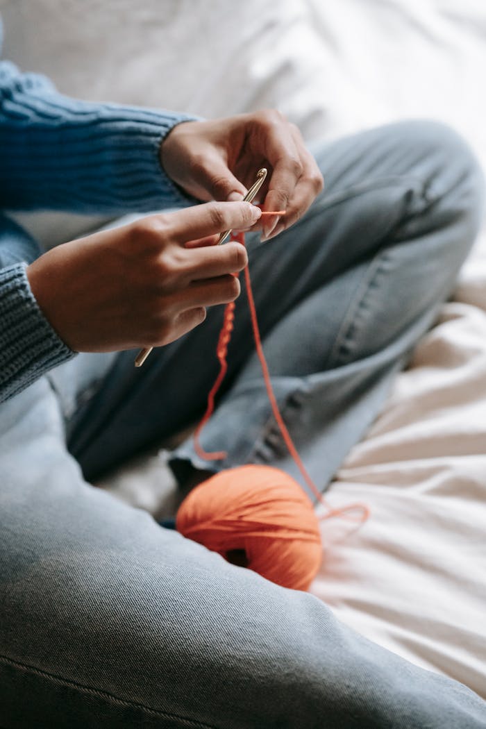 Detailed view of hands crocheting with orange yarn on denim jeans. Perfect for DIY and crafting themes.